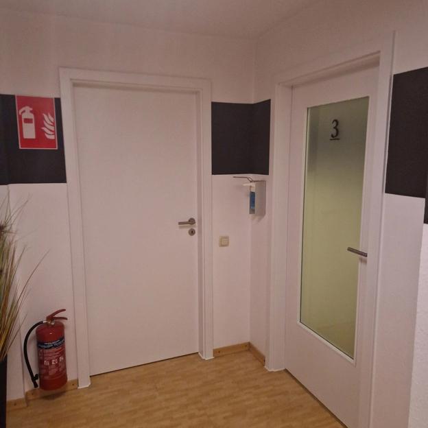 Moderne Praxistüren mit Glas und Raumkennzeichnung, daneben Feuerlöscher im Flur.