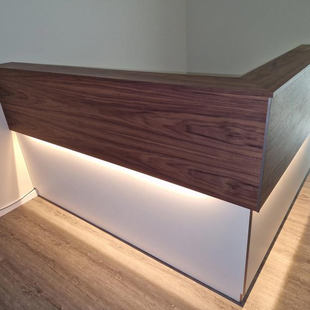 Moderne Empfangstheke mit Holzfront, weißem Unterbau und integrierter LED-Beleuchtung.