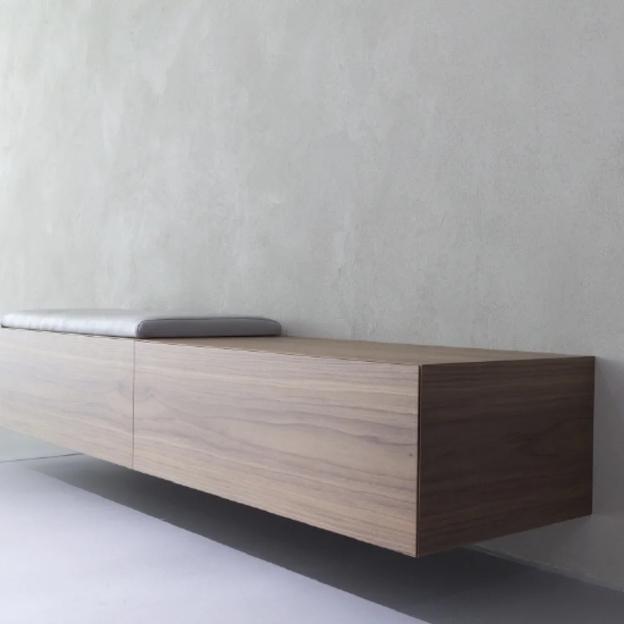 Schwebende Holzbank mit grauem Sitzpolster, minimalistisch an Wand montiert.