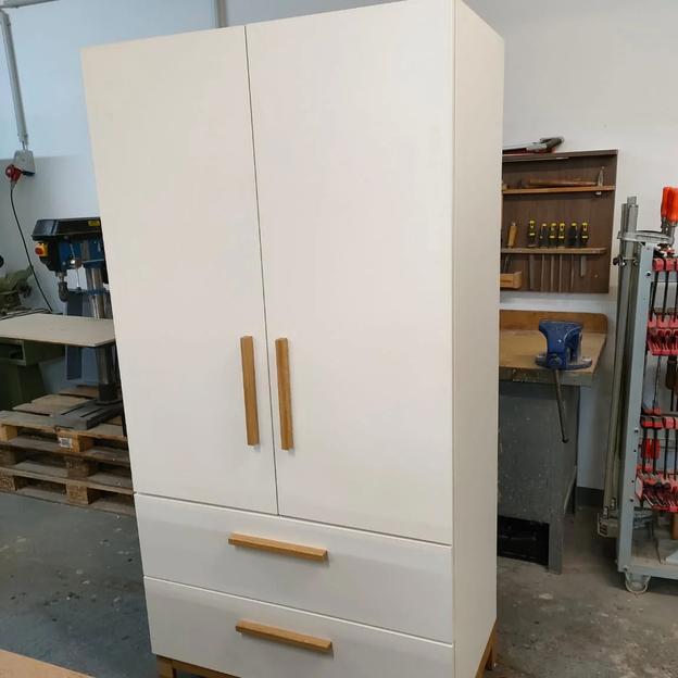 Weißer Schrank mit Holzgriffen und zwei Schubladen, gefertigt in einer Werkstatt.