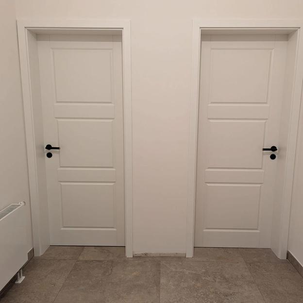 Zwei identische weiße Zimmertüren mit Kassettenoptik und schwarzen Türgriffen nebeneinander.