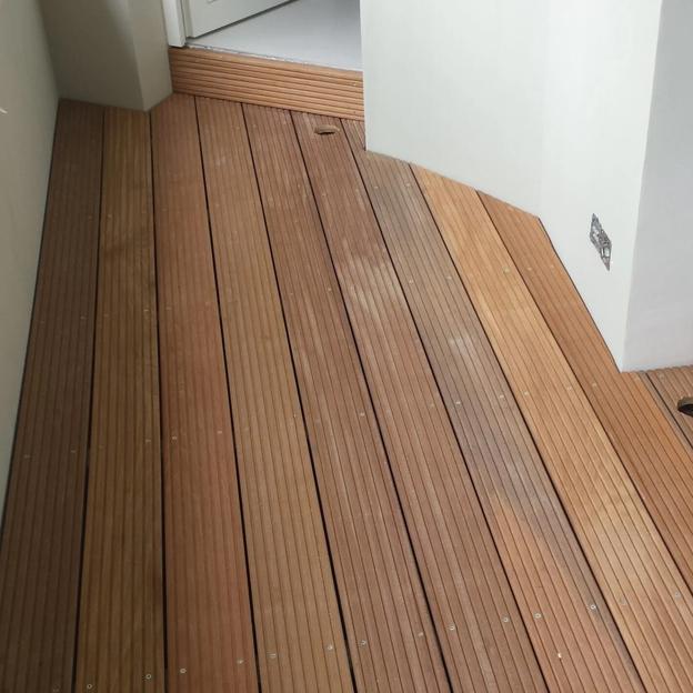 Schmale Holzterrasse mit gerillten Dielen, passgenau am Hauseingang verlegt.