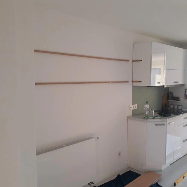 Lange Wandregale aus Holz in einer hellen Küche neben weißen Hängeschränken montiert.