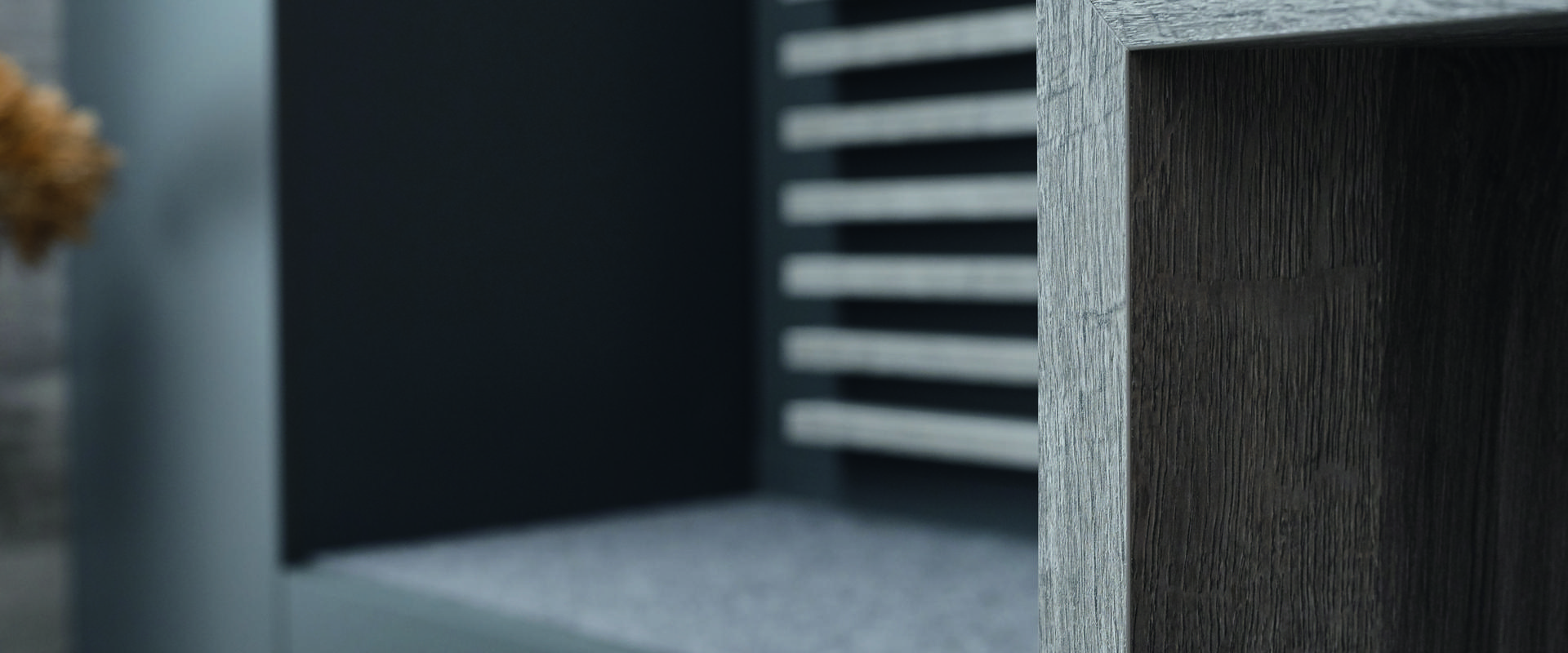 Detailaufnahme einer modernen Möbeloberfläche mit grauem Holzfurnier und strukturiertem Hintergrund.