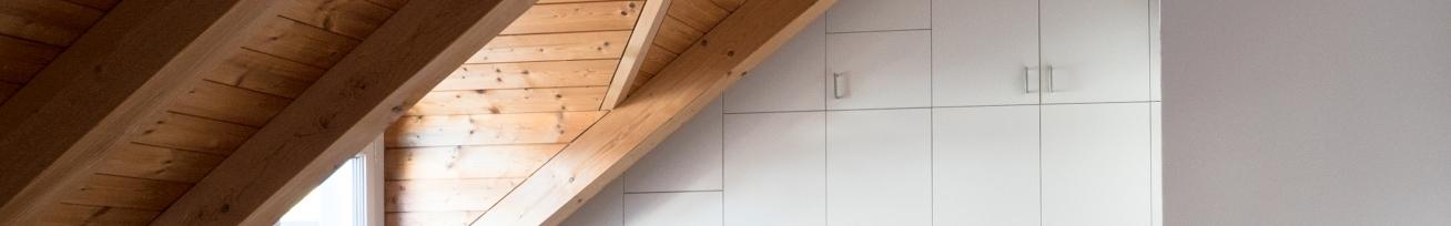 Nischenlösung für weißen Einbauschrank mit Schubladen und Türen an in dunklem Holz belassener Dachschräge